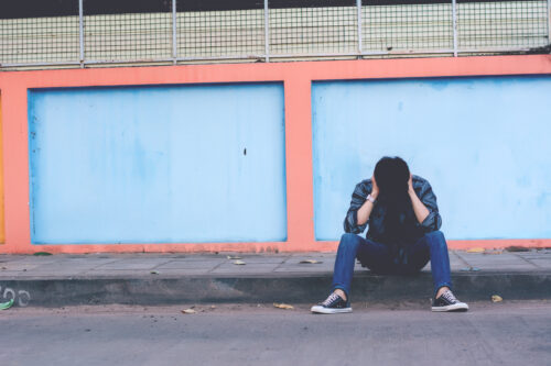 teen runaway sitting on curb with hands on head