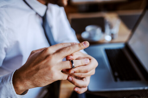 Unfaithful caucasian man in shirt and tie taking off his wedding ring. Selective focus on hand
