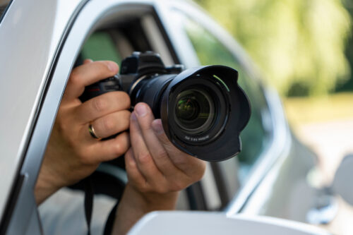 A paparazzi sits in his car and takes pictures of a famous person. Spy with camera in the car. A private detective, sitting inside the car, taking pictures with the camera.