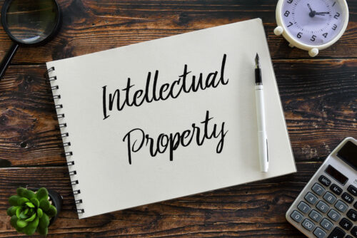 Top view of magnifying glass, plant,calculator,clock,pen and notebook written with Intellectual Property.