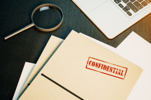 Top view of wooden desk top with laptop, magnifier and secret files. Confidential information and detective concept. 3D Rendering